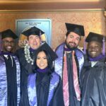 Five architecture students from NewSchool of Architecture of Design stand together and smile in their graduation cap and gowns.