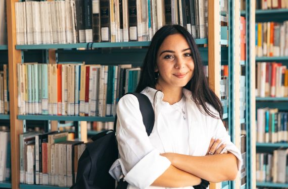 Design student grins while standing in front of books in school library