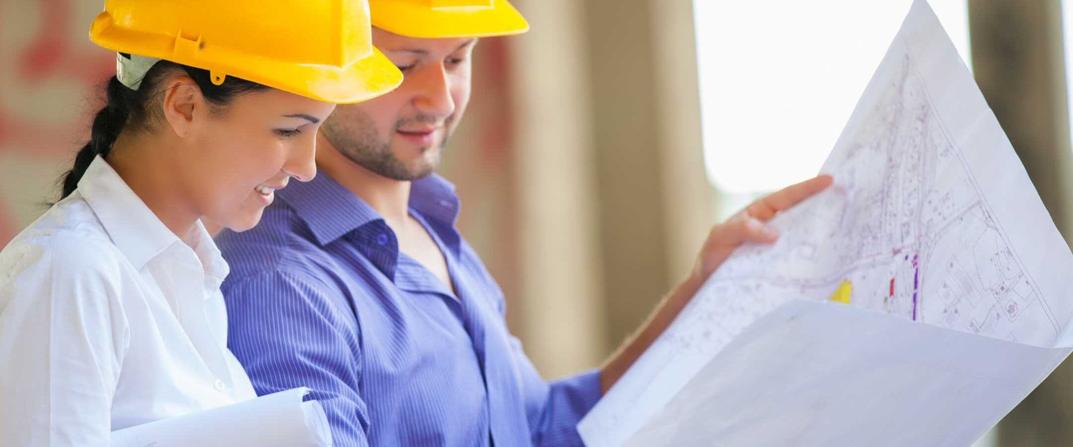 A woman and a man wearing construction hats look at blueprints together