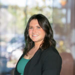 a close up of Izzy, wearing an emerald green blouse and smiling