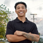 Cesar Tran, smiling with crossed arm showing tattoos and a black polo