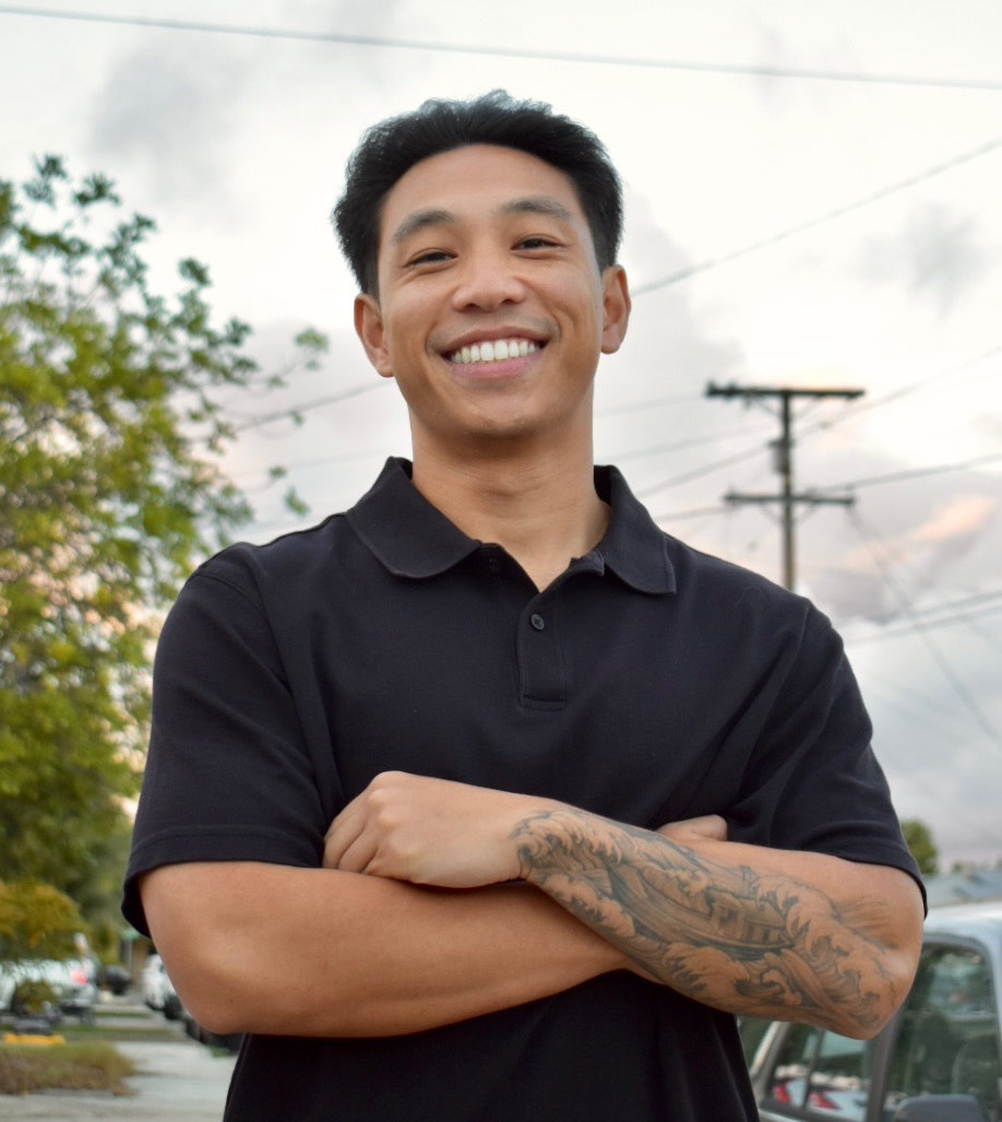 Cesar Tran, smiling with crossed arm showing tattoos and a black polo