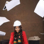Waldron Adebrah, wearing a white hard hat and smiling, surrounded by flynig papers