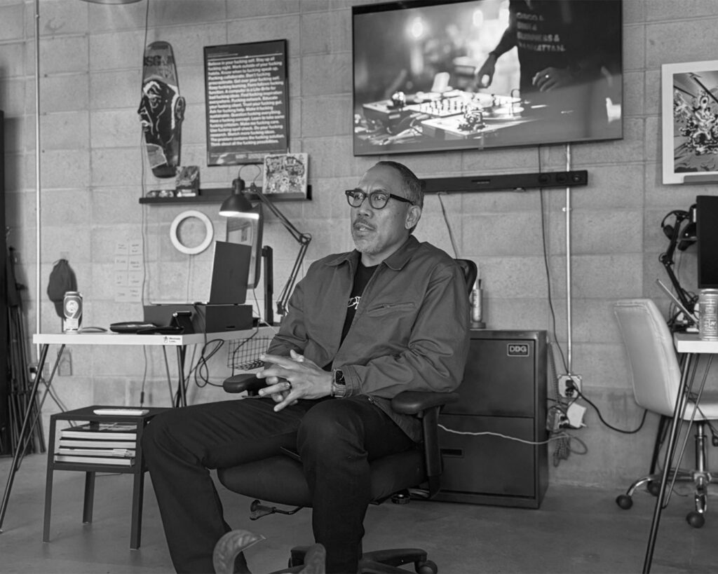 Allan Manzano sitting in a chair, speaking to others