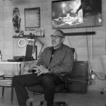 Allan Manzano sitting in a chair, speaking to others